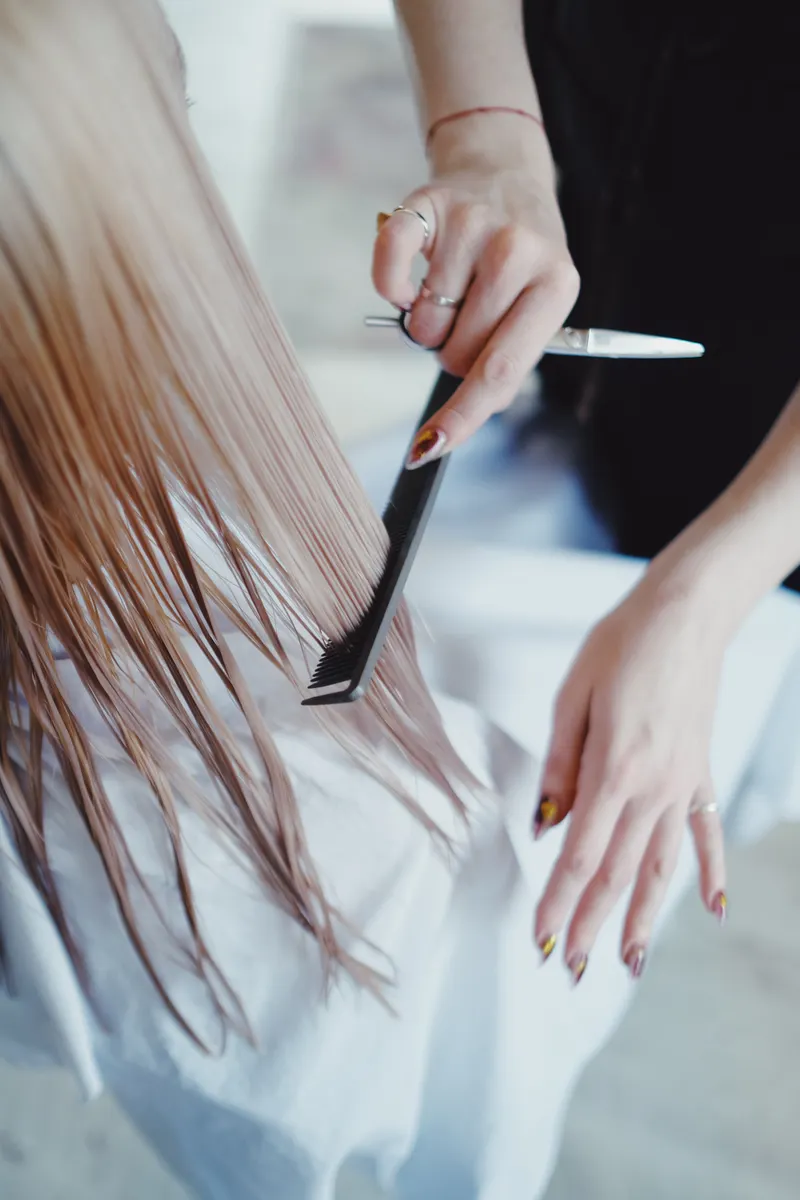 Estilista peinando una melena rubia con peine y tijeras